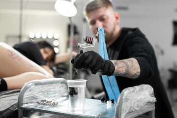 Tattoo master dips a tattoo machine with needle in water. Tattoo artist prepares tools and ink before work in tattoo parlor.