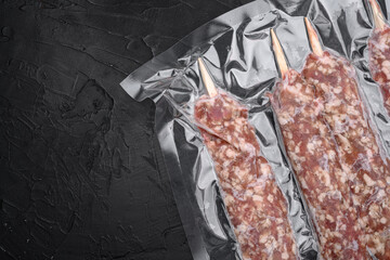 Vacuum packed raw meat skewers, on black dark stone table background, top view flat lay, with copy...