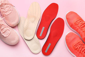 Orthopedic insoles and sportive shoes on pink background, closeup