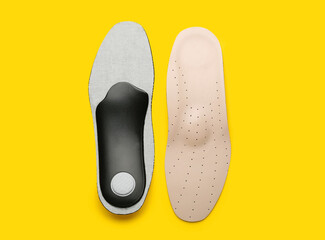 Pair of orthopedic insoles on yellow background