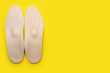 Pair of orthopedic insoles on yellow background