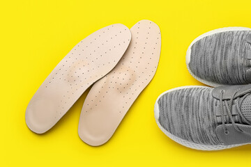 Pair of orthopedic insoles and sportive shoes on yellow background, closeup