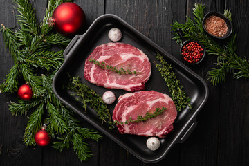 Raw rib eye beef steak with pepper and herbs to the Christmas and New Year, on black wooden table background, top view flat lay