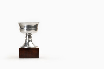Trofeo de acero de latón en forma de copa plateada con base de madera sobre un fondo blanco liso y...