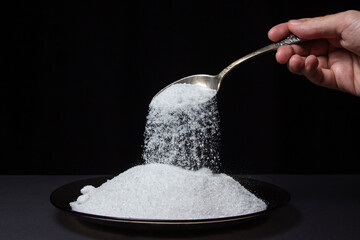 Salt is poured from a spoon onto a plate with salt on a black background. Excessive salt intake....