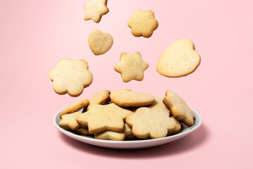 Cookies fall into a plate with cookies on a pink background. Homemade shortbread cookies. Delicious and light dessert.