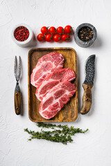 Raw pork neck chop meat with herb leaves and spice, on white stone table background, top view flat lay