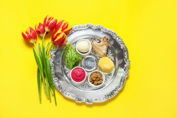 Passover Seder plate with traditional food and tulip flowers on color background