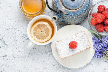 Breakfast or dessert with slice of cake, berries, teapot, cup of tea and spring flowers, top view. Spring concept