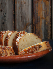 Slices of sweet bread with pieces of walnuts on top, over a mud or clay Mexican plate and a wooden wall as the  background, side view macro photography.