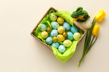 Basket with painted Easter eggs, tulip flowers and bunny on beige background