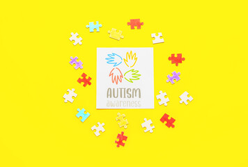 Paper sheet with text AUTISM AWARENESS, human palms and puzzle pieces on yellow background