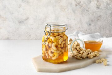 Board with jar of sweet cashew nuts in honey on grunge background