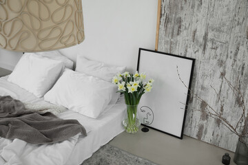Vase with daffodils and frame in light bedroom