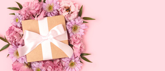 Banner with gift box with a tied bow and flower frame. Festive concept on a pink pastel background.