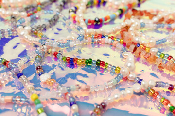 Fototapeta na wymiar Closeup of necklaces and bracelets made from colorful beads and pearls on a pink holographic background.