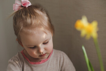 portrait of a little girl with yellow spring daffodil flower at home