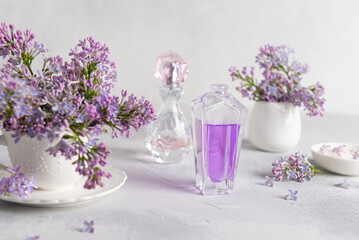 Obraz na płótnie Canvas Stylish bottle of lilac perfume with spray of lilac flowers on a white background. creative floral composition. Close up. Natural perfumery and floral scent concept. Fresh spring fragrant