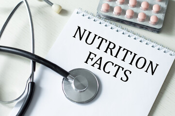 NUTRITION FACTS text on a notebook on a table next to a stethoscope and tablets, a medical concept