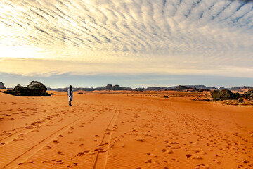 Fototapeta na wymiar Unrecognizable tuareg man standing in the sahara desert. Colorful sand, Rocky Mountains, sky with sunlight diffusing in stratus clouds.