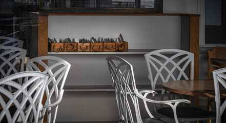 Cafe interior focusing on cutlery containers stacked on a shelf surrounded by white chairs.