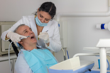 Obraz premium Middle-aged man is sitting on dentist chair with mouth opened while dentist is working on his ill tooth.