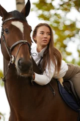 Foto op Canvas Beautiful young woman with horse outdoor. Concept of animal care. Rural rest and leisure. Idea of green tourism. Young european woman wearing uniform. © Georgii