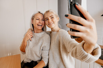 Blonde young happy mother and daughter at the kitchen making selfie for social network and having lots of fun. bloggering, family blog