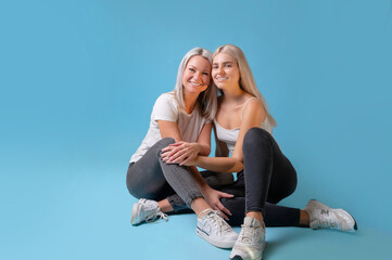 Blondehaired Mom and teenager daughter smiling on colorful backgroung. studio shoot with copy space