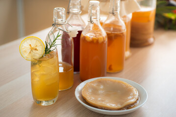 Kombu tea in a glass with ice, lemon slices and rosemary leaves, Homemade fermented raw kombucha tea in bottles and glass jars mix with fruit juice and scoby on table.Healthy natural probiotic drink.