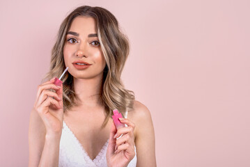 Beutiful blonde girl with natural makeup on light pink background, holding a lipstick , copy space
