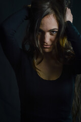 Fototapeta premium Portrait of a beautiful long-haired Italian woman who, with her hands on her head, has an intense and seductive gaze