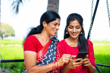 Relaxed mother and daughter on swing using mobile phone - concept of happiness, bonding, using...
