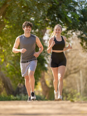 Young couple doing sports running on a park path and smiling