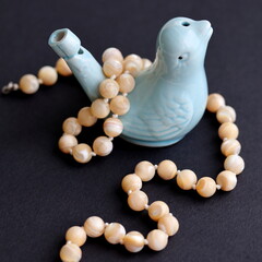 Mother of pearl nacre beads. Ceramic bird whistle figurine on black background.