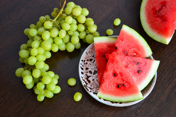 watermelon slices on plate with cluster of grapes on dark wooden background