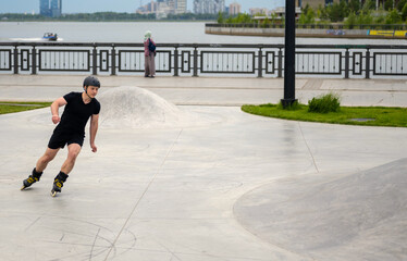Fototapeta premium man in black clothes skating in skates park on river and town background