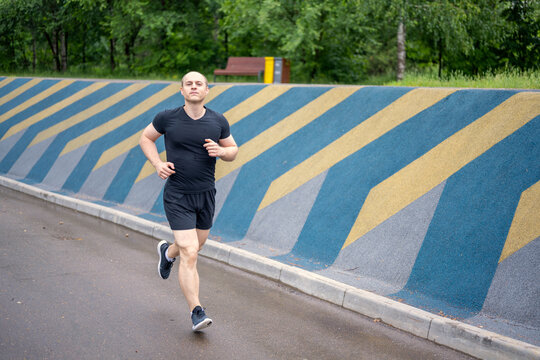 man in black clothes running in park in cloudy day on colored wall background