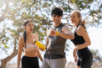 Three young people doing sports look at the smart watch and laugh in the park