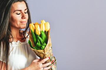 Attractive pleased  Lovable  Beautiful Smiling  Grateful  Woman receives flowers as present, stands with closed eyes, enjoys her favorite   Yellow, isolated on  purple background. Romantic portrait.