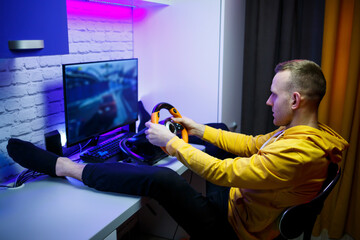Male gamer playing racing games on the computer. He uses the steering wheel. Emotional game