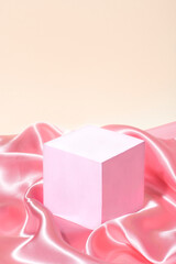 Cube podium on the calmy coral silk fabric, style of showcase for cosmetics product, display on pink (calmly coral) background, front view 