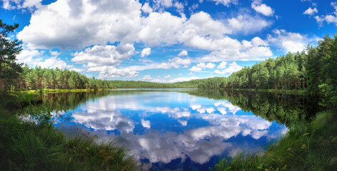 Beautiful natural morning landscape with a lake against backdrop of blue sky with clouds.