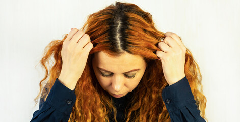 Close-up of the head of a red-haired girl with regrown dark roots. A woman shows her dark hair...