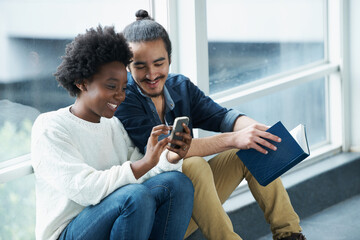What did she say. A college couple sitting closely together looking at a message on one of their phones.