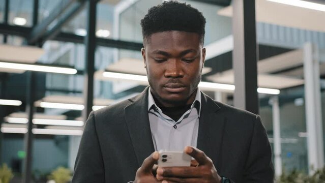 Serious young man african american office worker searching smartphone internet choosing making order chatting online with friends scrolling mobile phone thoughtful male user click at browser account