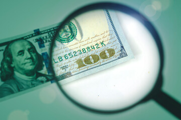 Magnifying glass on the background of a 100 dollars close-up. Hand holding loupe for dollar...