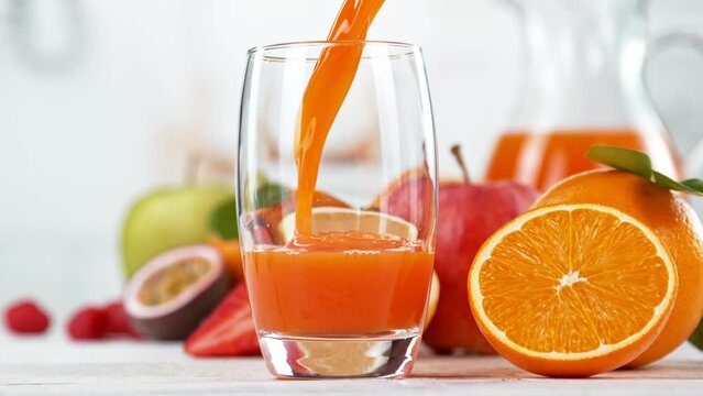 Super slow motion of pouring multivitamin juice into glass. Placed on white table with kitchen on background. Filmed on high speed cinema camera, 1000 fps.