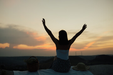 The young woman sitting on the mountain with her hands up at the sunset, turned out to be happy and free.