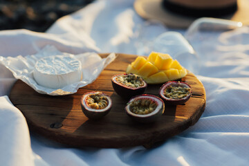 Beautiful summer picnic at sunset with brie cheese, mango and passion fruits.